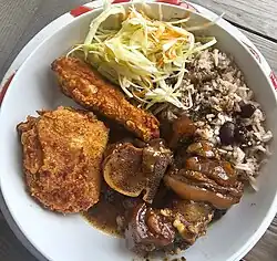 Brown stew pork and fried chicken, served with rice and peas and vegetables.