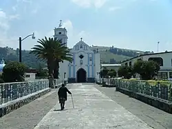A person walks down a street in Joquicingo de León Guzmán with a church in the background.