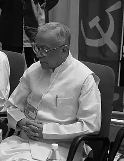 Greyscale image of an old Indian man, wearing a dhoti and kurta, and looking down.