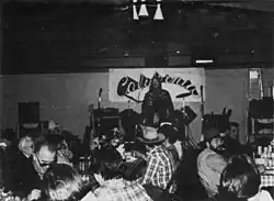 Man with mustache speaking to a seated audience in what appears to be an office setting