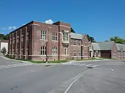 A two-story brick building extends from the foreground off to the right side of the frame. A road runs before it. The day is sunny and clear.