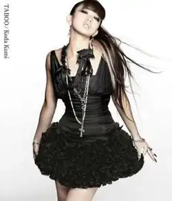 A woman, dressed in a black dress with black-coloured accessories, posing towards the camera with blonde streaks in her hair. The text "Koda Kumi", and "Taboo" are placed on the upper-left side of the image.