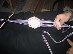 No shuttle; just passing a ball of yarn through the shed. Tablet weaving, Finland.