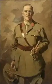 Painting of man in khaki uniform wearing a Sam Browne belt, jacket with two rows of ribbons and red tabs, and a tie. He is holding a slouch hat with emu feathers in one hand, and a swagger tucked under his left arm.