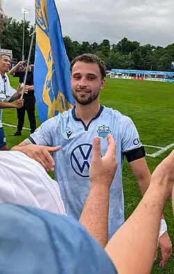 Player approaching fans, hand extended, while someone waves a flag behind him