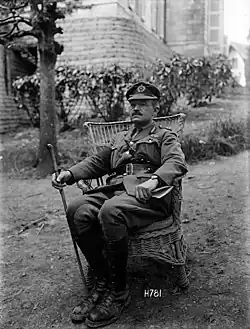 A black and white photograph of a man wearing military uniform seated on a garden chair on a lawn
