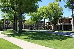 Photo of green trees on campus with a building and library.