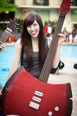 A woman, dressed in a grey shirt holding a red axe-bass hybrid.