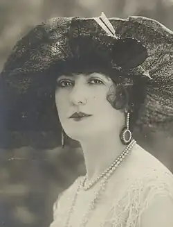 A portrait of Marcelle Praince, wearing a large hat and drop earrings