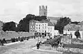 a mono-chrome photo of citizens sitting on, and looking from a road bridge, with a church in the background