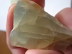 A chunk of grayish yellow moonstone which shows fracture lines and a blue glow in some portions.
