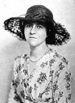 Nan Bagby Stephens, a white woman wearing a dark lacy brimmed hat and a floral-print dress