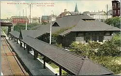 A postcard showing a one-story Romanesque train station next to below-grade tracks