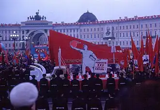 A group of people waving various red flags surrounding a parade float with communist and Soviet symbolism.
