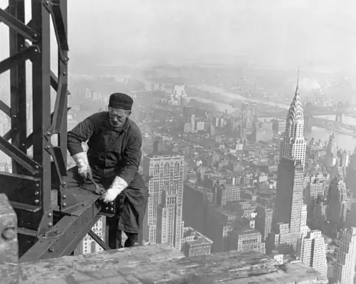A man working on a steel girder high above a city skyline.