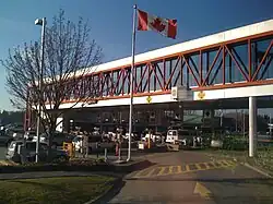 An overhead walkway is above several rows of cars waiting to cross the border