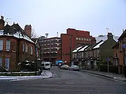 A tall red brick building towers over streets of two-storey houses. The roofs of the houses and the surrounding pavements are covered in snow.