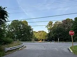 Intersection with a stop sign, surrounded by trees, with a playground and strip mall in the distance
