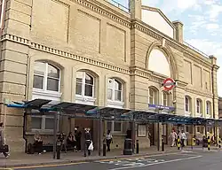 A beige-bricked building with a rectangular, dark blue sign reading "PUTNEY BRIDGE STATION" in white letters all under a light blue sky