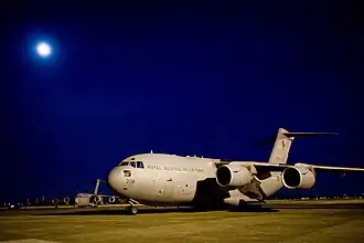 Four-engined military jet transport plane parked on airfield at night with moon overhead