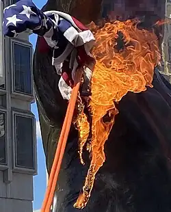 The statue graffitied and with a burning American flag attached to it with a rope
