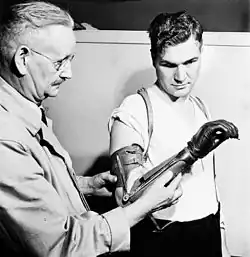 Ronny Jaques: Private Ed Gerris of the Royal Canadian Army Service Corps, with Principal Eccles of Shaw Business Schools, is using a specially designed glove-covered artificial hand to learn penmanship during a retraining course on Primary Accountancy, 1944