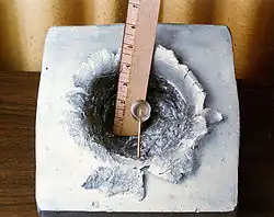 A 7-gram object (shown in centre) shot at 7&nbsp;km/s (23,000&nbsp;ft/s), the orbital velocity of the ISS, made this 15&nbsp;cm (5.9&nbsp;in) crater in a solid block of aluminium.