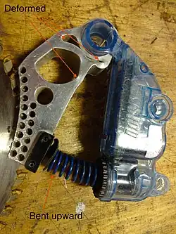 Saw braking cartridge after activation. The aluminum frame has been crushed as a result of impact by the moving saw blade, and the spring stretched.