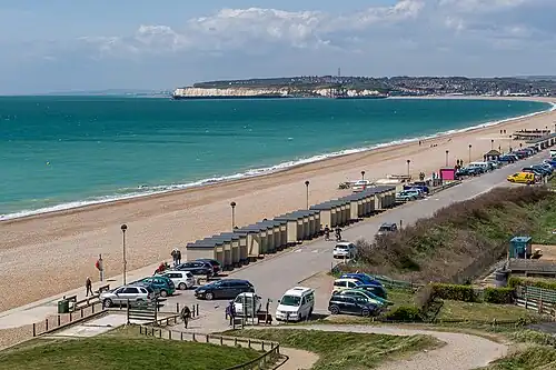 A photograph of the sea and a curved sandy beach with a chalk headland in the distance