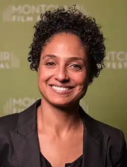 Lynch is a middle aged woman with light brown skin, short curly hair, and is smiling at the camera.