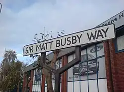 A white road sign with a black border and the words "Sir Matt Busby Way" in black capital letters.