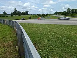 Three solar cars enter the downhill to the "sinkhole" feature at the National Corvette Museum Motorsports Park during Electrek FSGP 2024. Leading is car #828 from Appalachian State - a two seater car in the MOV Class. Behind them are two cars in the SOV class: #5 from the University of Florida and #6 from Berkeley.