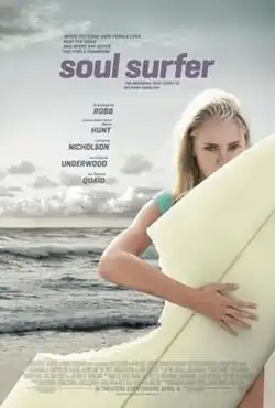 A teenage girl holds a surfboard at the beach. A section of her board is missing as if been bitten by a shark