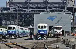 A train yard with several idle trains parked on various tracks in front of a barn with the Amtrak logo.