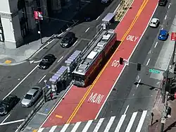 Overhead view of an urban arterial with red center lanes and a bus platform, with a bus at the platform