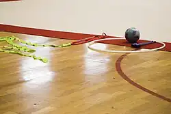 A ribbon, folded rope, hoop, ball, and pair of clubs on the ground outside the gymnastics floor