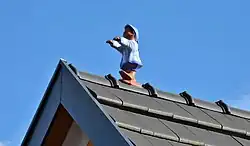 A cartoonish figure looks like it is walking along the ridge of the roof and may fall off in a few more steps