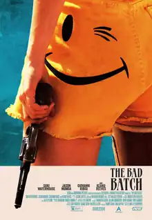 A close-up of a woman's arm holding a gun resting next to her side, and her yellow shorts designed with a winking smiley face on her left side.