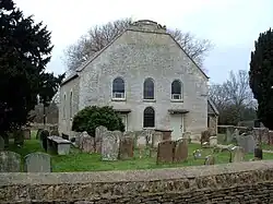 A grey-white building seen almost end-on with two storeys. The lower storey has two doors with a round-headed window between, the upper storey has three round-headed windows, and at the top is a truncated gable.