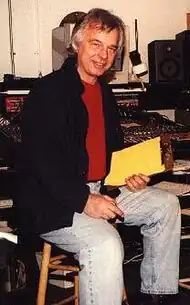 A grey-haired man with glasses and a black shirt standing in front of a microphone