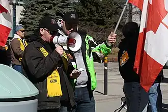 Two USW workers are pictured attending a protest during the 2009–2010 Vale Inco strike. One speaks into a megaphone while the person beside them holds a Canadian flag.