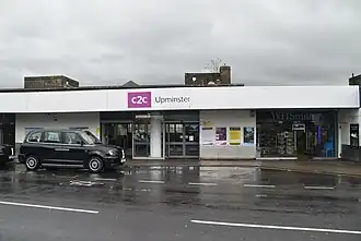 Wide station frontage with station sign above entrance and a taxi cab outside