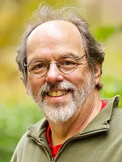Portrait of Ward Cunningham, a middle-aged bearded man, wearing wire rim eyeglasses and an olive drab fleece jacket