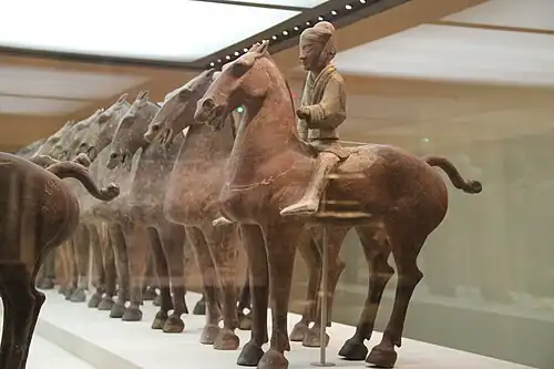 Various ancient ceramic models of soldiers on horseback behind glass in a museum display