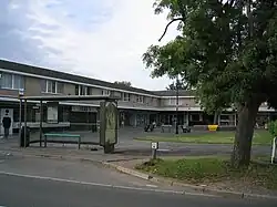 Row of shops in pedestrianised precinct. In the foreground a bus shelter and tree.