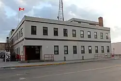 The post office seen from the other street it faces, with its entrance on the ground floor at left, the flag flying, and sunlight coming through the clouds behind it